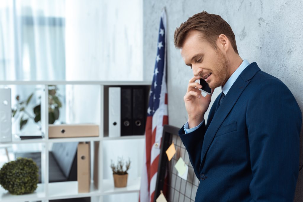 cheerful young businessman in suit talking on smartphone in modern office
